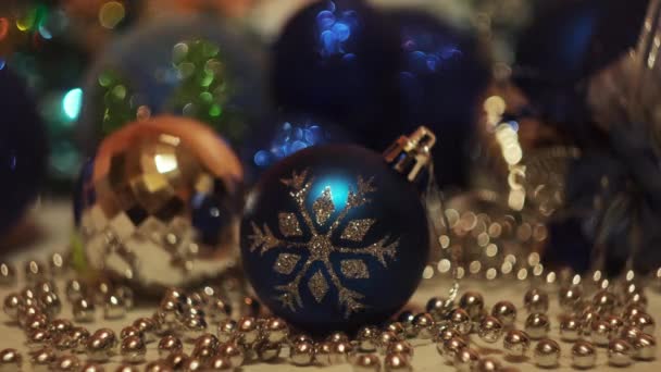 Kerst speelgoed op feestelijke knipperende lichten achtergrond. Concept. Nieuwjaarsvakantie, close-up van mooie blauwe speelbal met een sneeuwvlok en glanzende bloemenslinger.  - Video