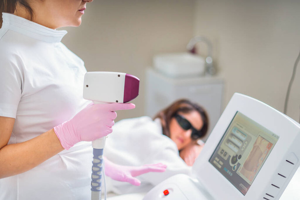 kobieta w profesjonalnej klinice kosmetycznej podczas laserowej depilacji. Leczenie depilacyjne. Koncepcja gładkiej skóry - Zdjęcie, obraz