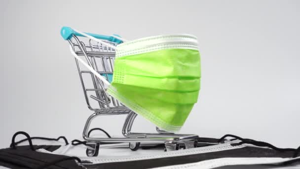 Carro de supermercado con colorida máscara médica protectora verde en una pila de máscaras de higiene negro. De cerca. Dolly disparó. Miniatura conceptual - Imágenes, Vídeo