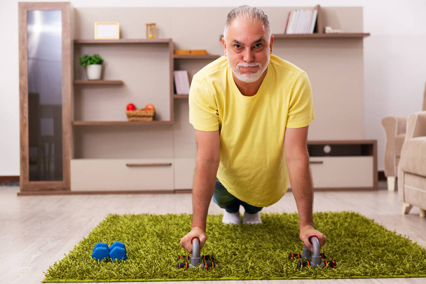 Az idős férfi otthon sporttevékenységeket végez. - Fotó, kép