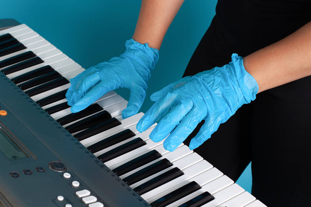 close-up of female hands and fingers in rubber medical gloves playing a melody on an electronic synthesizer, side view isolated on a blue background - Foto, Imagen