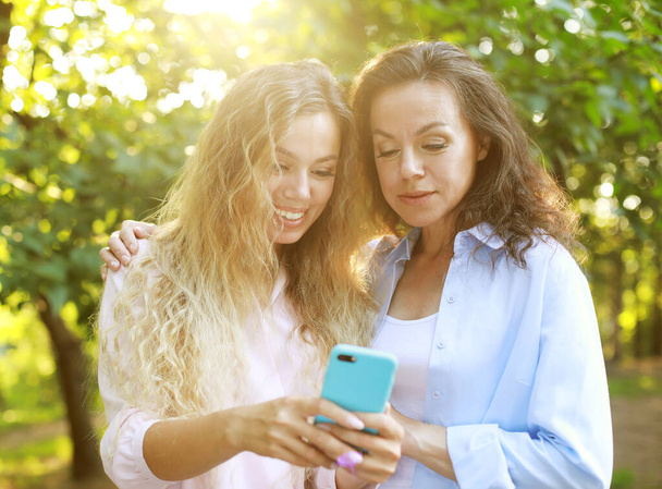 Portrait of Adult caucasian daughter showing on mobile phone to her senior mother outdoor in nature - Photo, image