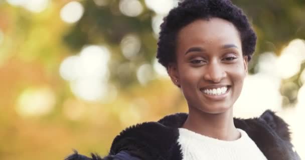 Πορτρέτο της όμορφης ελκυστική θετική αφρικανική αμερικανική κορίτσι στέκεται μόνη της απομονωμένη σε εξωτερικούς χώρους το φθινόπωρο φοράει μαύρο μπουφάν εξωτερικά χαμόγελα χαμόγελο ευρύ toothy κοιτάζει κάμερα αιωρείται σε διαφορετικές πλευρές - Πλάνα, βίντεο