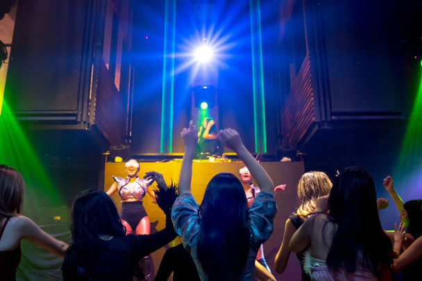 Группа людей танцует в дискотечном ночном клубе под ритм музыки от DJ на сцене - Фото, изображение