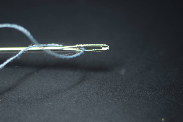 Macro fotografía de aguja de coser. Aguja pequeña con hilo en el ojal, aislada sobre el fondo negro. - Foto, Imagen