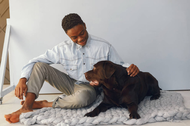 Handsome black man sitting on a blue background with a dog - 写真・画像
