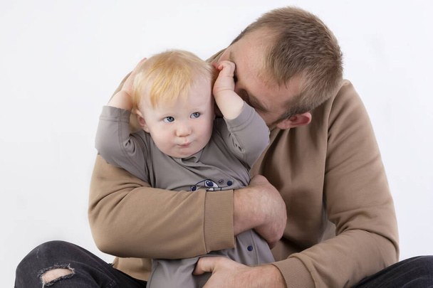 На сірому тлі тато ніжно цілує свого однорічного сина. Батько і маленький син
. - Фото, зображення