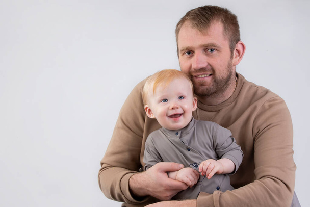 Em um fundo cinza, um retrato de um pai e um pequeno filho sorridente de um ano. - Foto, Imagem