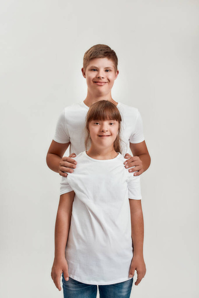 Two kids, disabled boy and girl with Down syndrome smiling at camera while posing together isolated over white background - Fotografie, Obrázek