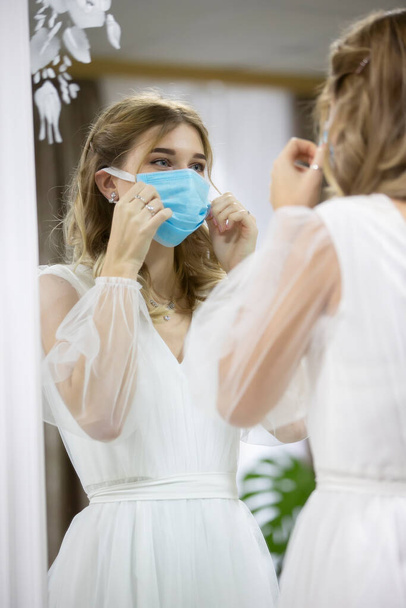 A noiva na máscara médica olha no espelho. - Foto, Imagem
