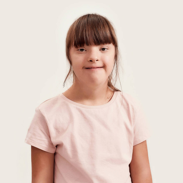 Close up portrait of disabled girl with Down syndrome smiling at camera while posing isolated over white background - Φωτογραφία, εικόνα