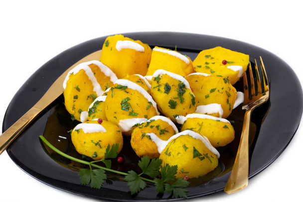 Mit Kräutern bestreute Bratkartoffeln auf einem schwarzen Teller. - Foto, Bild