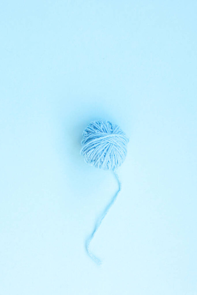 Een blauwe bal van wollen draad met lange gedraaide draad op een lichtblauwe achtergrond met kopieerruimte - Foto, afbeelding