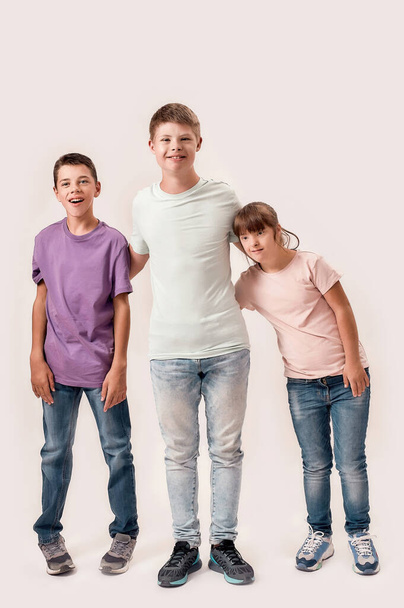Полнометражный снимок трех веселых подростков-инвалидов с синдромом Дауна и церебральным параличом, улыбающихся стоя вместе на белом фоне - Фото, изображение