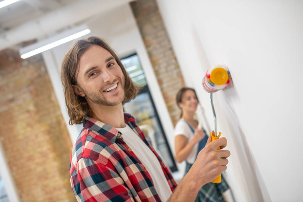 Young man with paint roller in his hand painting wall - Photo, Image