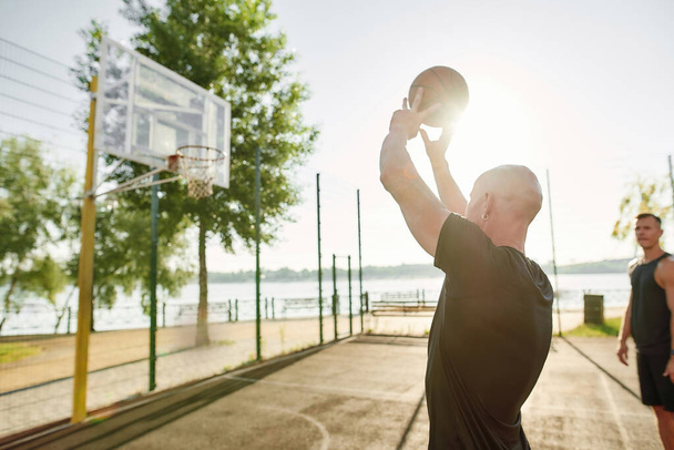 Close up of man holding basketball while playing outdoors together with his friends on a sunny day - Foto, immagini