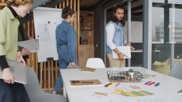 PAN shot van team van jonge creatieve start-up medewerkers lopen in de vergaderzaal in modern kantoor en het openen van hun laptops, dan bespreken project - Video