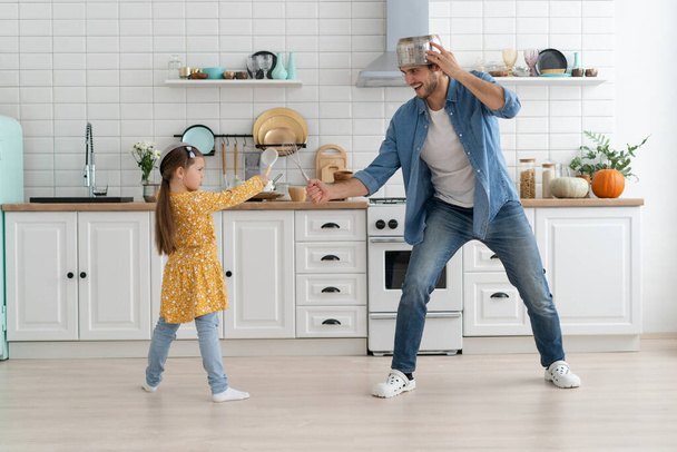 Caucasian father and daughter enjoy battle funny activity in kitchen spend active time together on weekend at home - Fotoğraf, Görsel