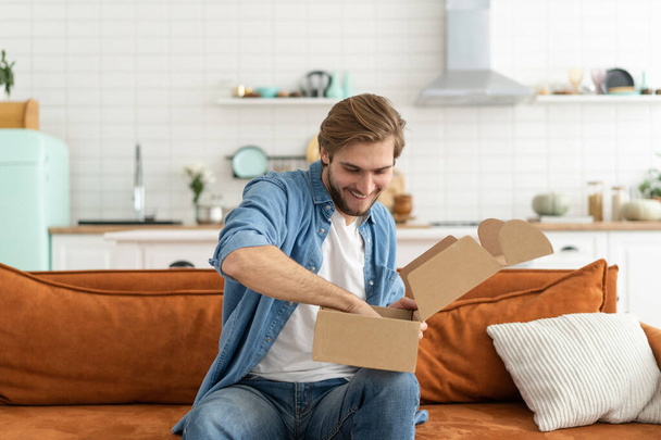 Happy man customer unpacking cardboard box receive open post mail delivery package - Fotó, kép