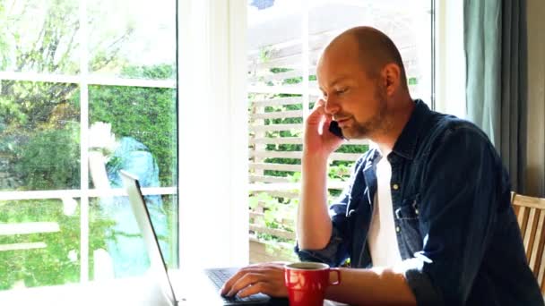 Mężczyzna rozpoczynający, prowadzący i kończący rozmowę przez telefon podczas pracy nad laptopem. - Materiał filmowy, wideo