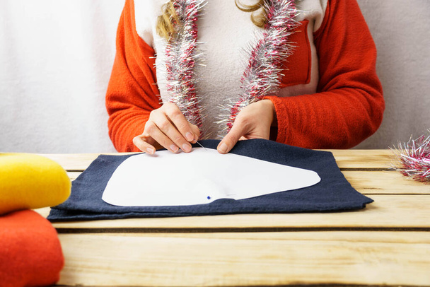 A lány karácsonyi törpét varr. Egy 30-35 éves lány télapó kalapot visel, és a saját kezével készít játékot. Karácsonyi háttér. - Fotó, kép