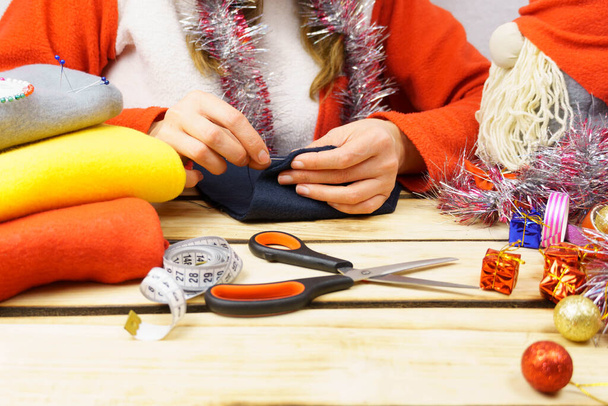 Het meisje naait een kerstkabouter. Een meisje van 30-35 jaar met een kerstmuts op maakt speelgoed met haar eigen handen. Kerst achtergrond. - Foto, afbeelding