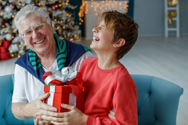 Παππού και εγγόνια σε ένα δωμάτιο διακοσμημένο για τα Χριστούγεννα στο φόντο ενός χριστουγεννιάτικου δέντρου. Χριστουγεννιάτικη ιδέα διακοπών. φωτογράφηση αντίθεσης. - Φωτογραφία, εικόνα