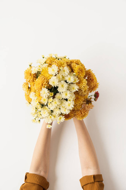 Flatlay of yellow and ginger fall wild flowers bouquet in women's hands isolated on white background. Flat lay, top view minimalistic floral composition. Valentine's Day, Mother's Day concept. - Photo, Image
