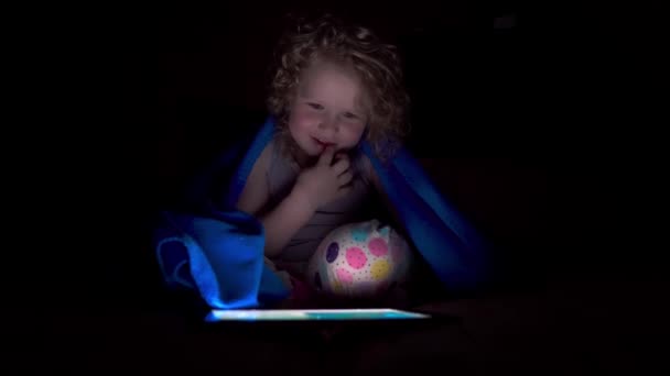 Küçük kız yatakta battaniyenin altında oturuyor ve bir video görüşmesi yapıyor.. - Video, Çekim