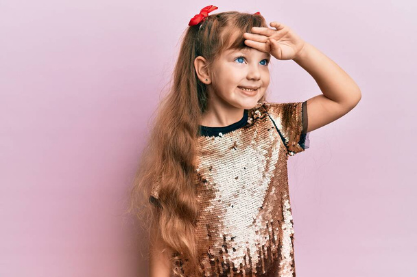 Little caucasian girl kid wearing festive sequins dress very happy and smiling looking far away with hand over head. searching concept.  - Photo, Image