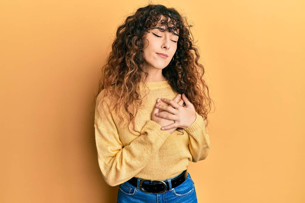 Young hispanic girl wearing casual clothes smiling with hands on chest with closed eyes and grateful gesture on face. health concept.  - 写真・画像