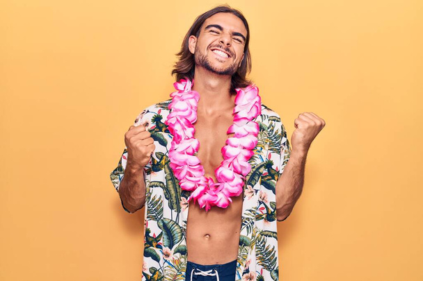 Mayo giyen genç yakışıklı bir adam ve Hawaii zambağı çok mutlu ve heyecanlı kollarını kaldırıp, gülümseyerek ve başarı için bağırarak kazanan jestler yapıyor. kutlama konsepti.  - Fotoğraf, Görsel
