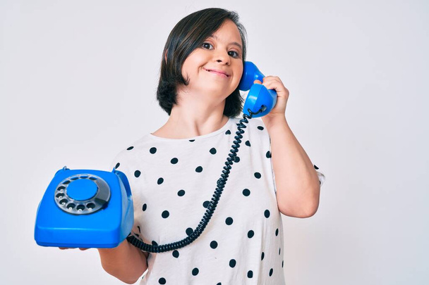 Brünette Frau mit Down-Syndrom hält Telefon in der Hand, lächelt zur Seite und starrt nachdenklich weg.  - Foto, Bild
