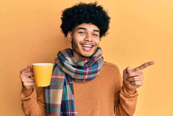 Young african american man with afro hair drinking a cup of coffee smiling happy pointing with hand and finger to the side  - Foto, immagini