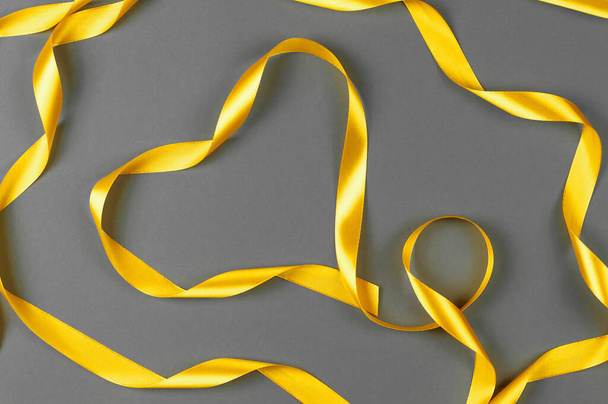 Κίτρινο σατέν κορδέλα σε γκρι φόντο.Track χρώματα 2021. - Φωτογραφία, εικόνα