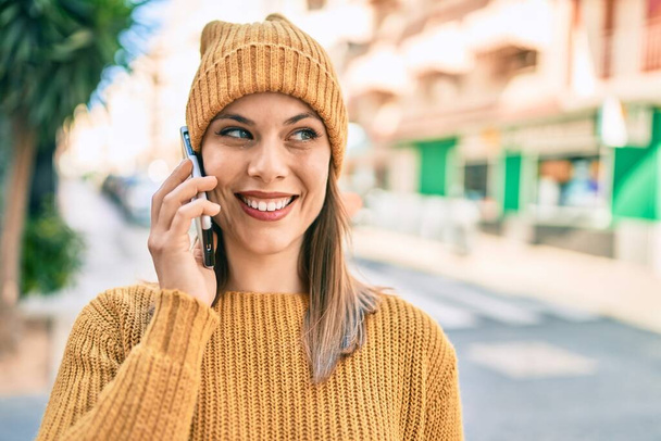 Nuori blondi nainen hymyilee onnellinen käyttäen älypuhelinta kaupungissa. - Valokuva, kuva