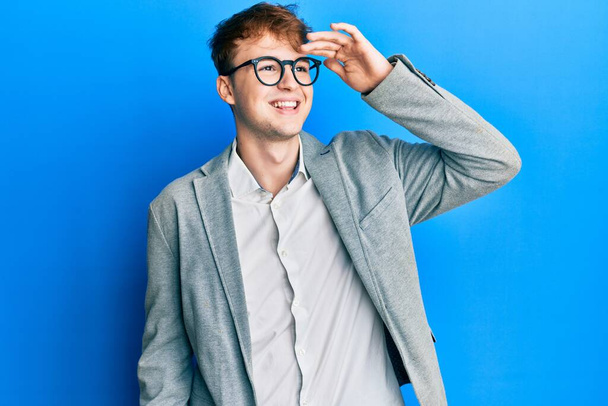 Giovane uomo caucasico indossa abiti eleganti e occhiali molto felice e sorridente guardando lontano con mano sopra la testa. concetto di ricerca.  - Foto, immagini