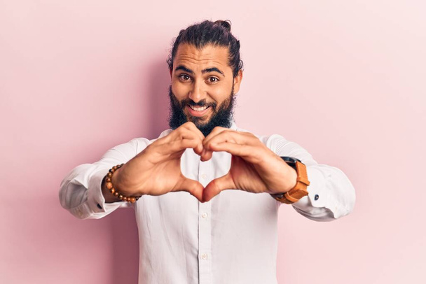 Junger arabischer Mann in lässiger Kleidung, verliebt lächelnd und mit Händen in Herzsymbolform. Romantisches Konzept.  - Foto, Bild