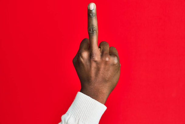Рука і рука афроамериканського чорного чоловіка над червоним, ізольованим фоном, що показує провокативний і грубий жест робить трахкав тебе символом середнього пальця.  - Фото, зображення