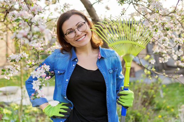 Spring gardening, portrait of mature smiling woman with rake looking at camera - Fotó, kép