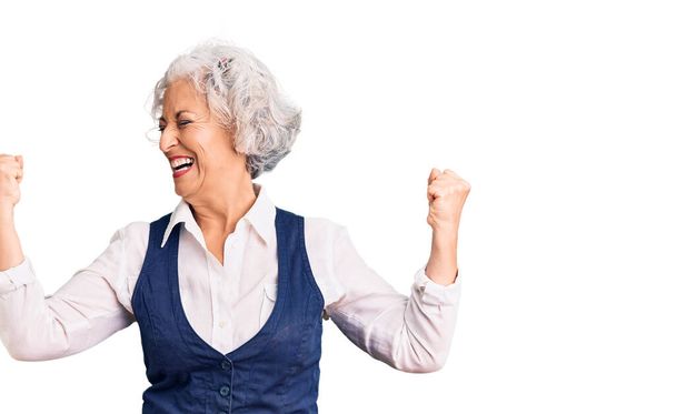 Starsza siwowłosa kobieta ubrana w luźne ubrania bardzo szczęśliwa i podekscytowana wykonując gest zwycięzcy z podniesionymi ramionami, uśmiechnięta i krzycząca o sukces. koncepcja uroczystości.  - Zdjęcie, obraz