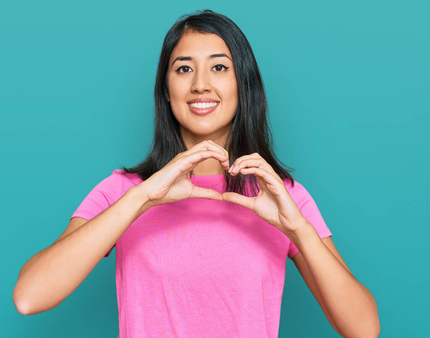 Piękna azjatycka młoda kobieta ubrana w luźny różowy t-shirt uśmiecha się w miłości robi kształt symbolu serca z rąk. romantyczna koncepcja.  - Zdjęcie, obraz
