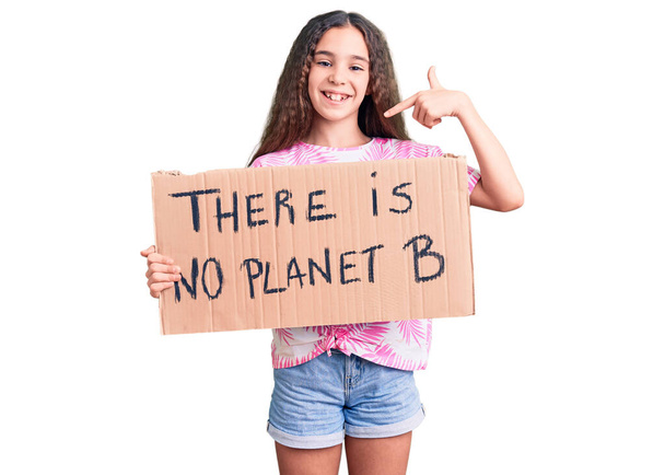 Schattig hispanic kind meisje houden er is geen planeet b banner wijzend vinger naar een zelf glimlachend gelukkig en trots  - Foto, afbeelding