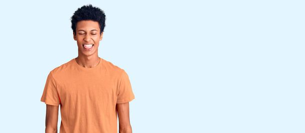 若いアフリカ系アメリカ人の男性が面白い表情で幸せ舌を突き出してカジュアルな服を着ています。感情の概念.  - 写真・画像