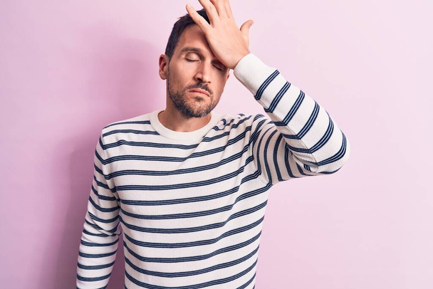 Young handsome man wearing casual striped sweater standing over isolated pink background surprised with hand on head for mistake, remember error. Forgot, bad memory concept. - Foto, Imagen