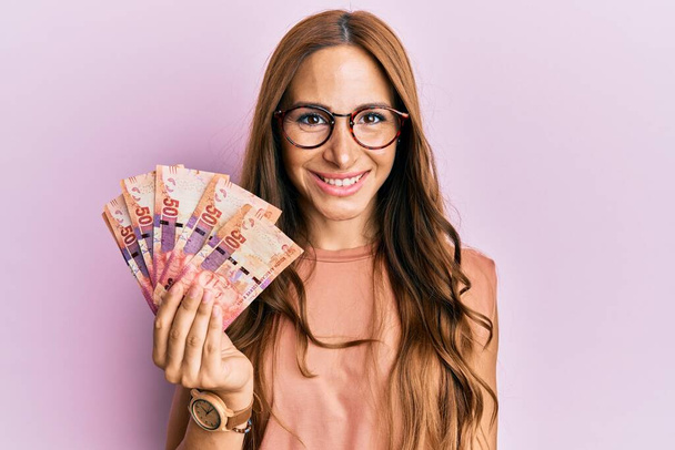 若いですブルネット女性保持南アフリカのブランドの紙幣見て正と幸せな立ちと笑顔で自信を持って笑顔示す歯  - 写真・画像