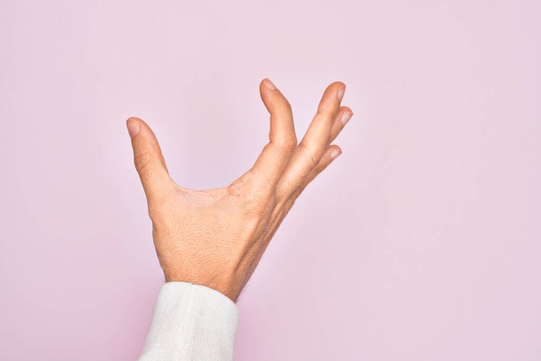 Χέρι του Καυκάσου νεαρός άνδρας δείχνει τα δάχτυλα πάνω από απομονωμένο ροζ φόντο συλλογή και τη λήψη αόρατο πράγμα, κρατώντας αντικείμενο με τα δάχτυλα που δείχνουν χώρο - Φωτογραφία, εικόνα