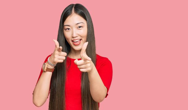 Jeune femme chinoise portant des vêtements décontractés pointant les doigts vers la caméra avec un visage heureux et drôle. bonne énergie et vibes.  - Photo, image
