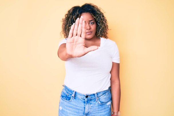 Junge afrikanisch-amerikanische Plus-Size-Frau in lässigem weißem T-Shirt beim Stop-Singen mit der Handfläche. Warnausdruck mit negativer und ernster Geste im Gesicht.  - Foto, Bild