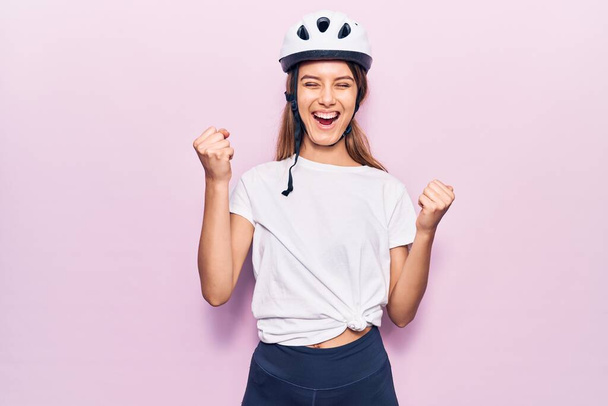 Bisiklet kaskı takan genç ve güzel bir kız şaşkınlık ve şaşkınlık içinde kollarını kaldırarak ve gözlerini kapatarak başarıyı kutluyor.  - Fotoğraf, Görsel